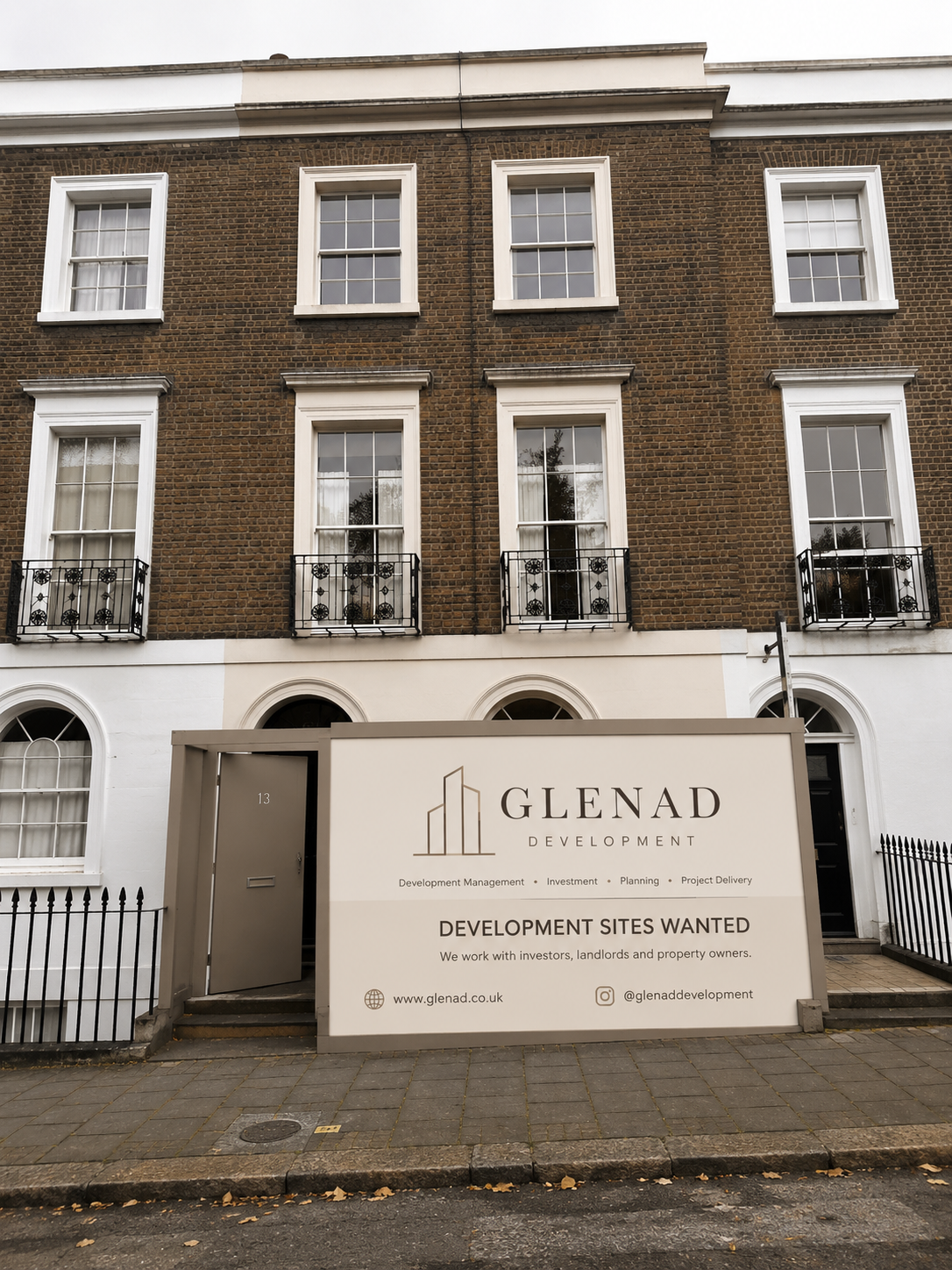 A large sign in front of a multi-story brick building with white window trim and small balconies. The sign is for Glenad Development and indicates they are seeking development sites, working with investors, landlords, and property owners.