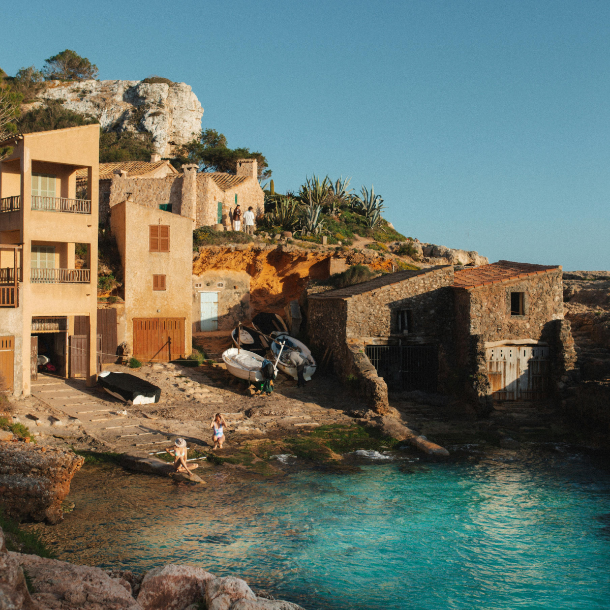 a mallorca spain beach at sunset with turquoise water and a stucco colored home
