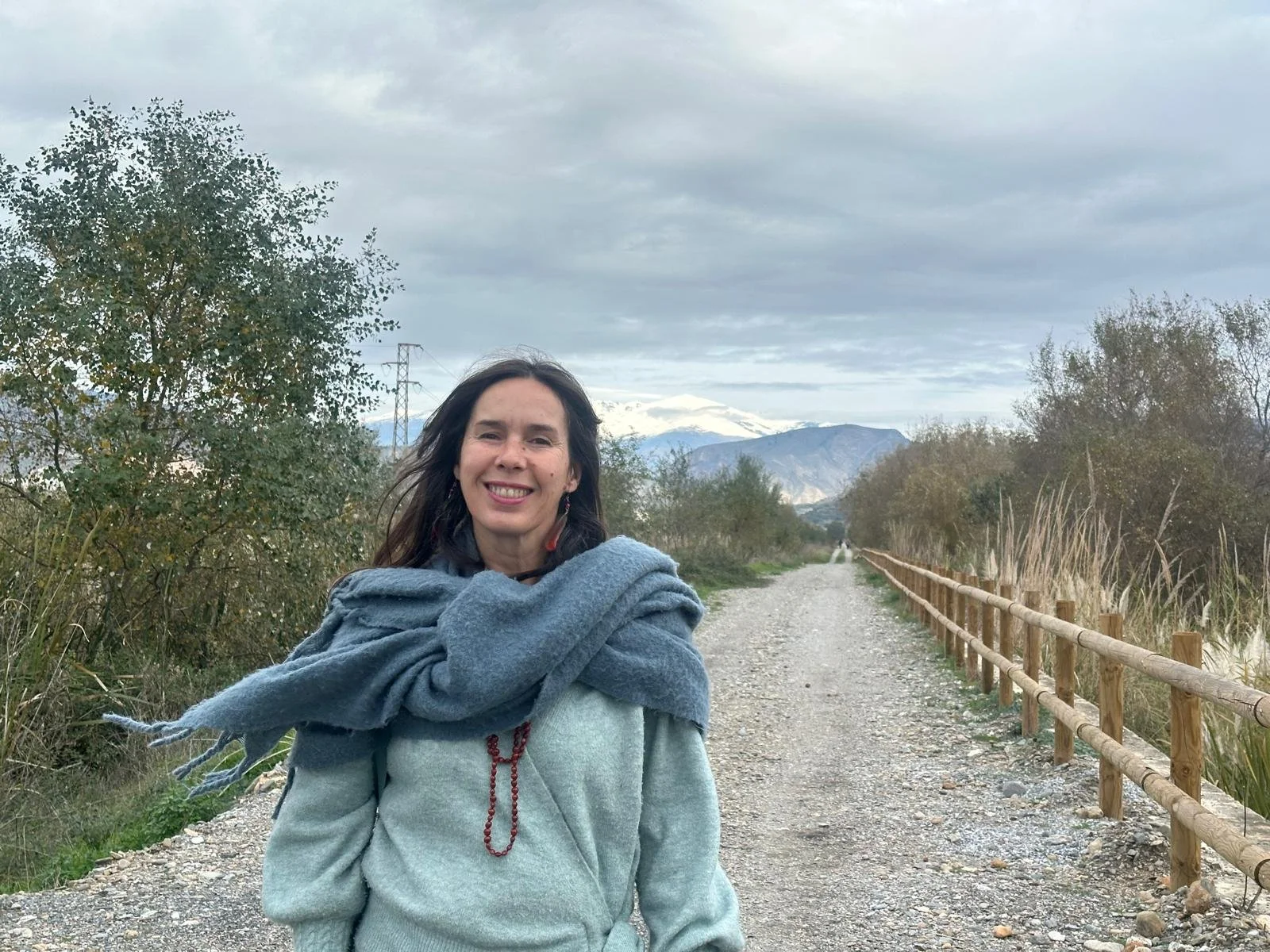 Fotografía de Carmen Sánchez en un sendero, con montañas nevadas al fondo.