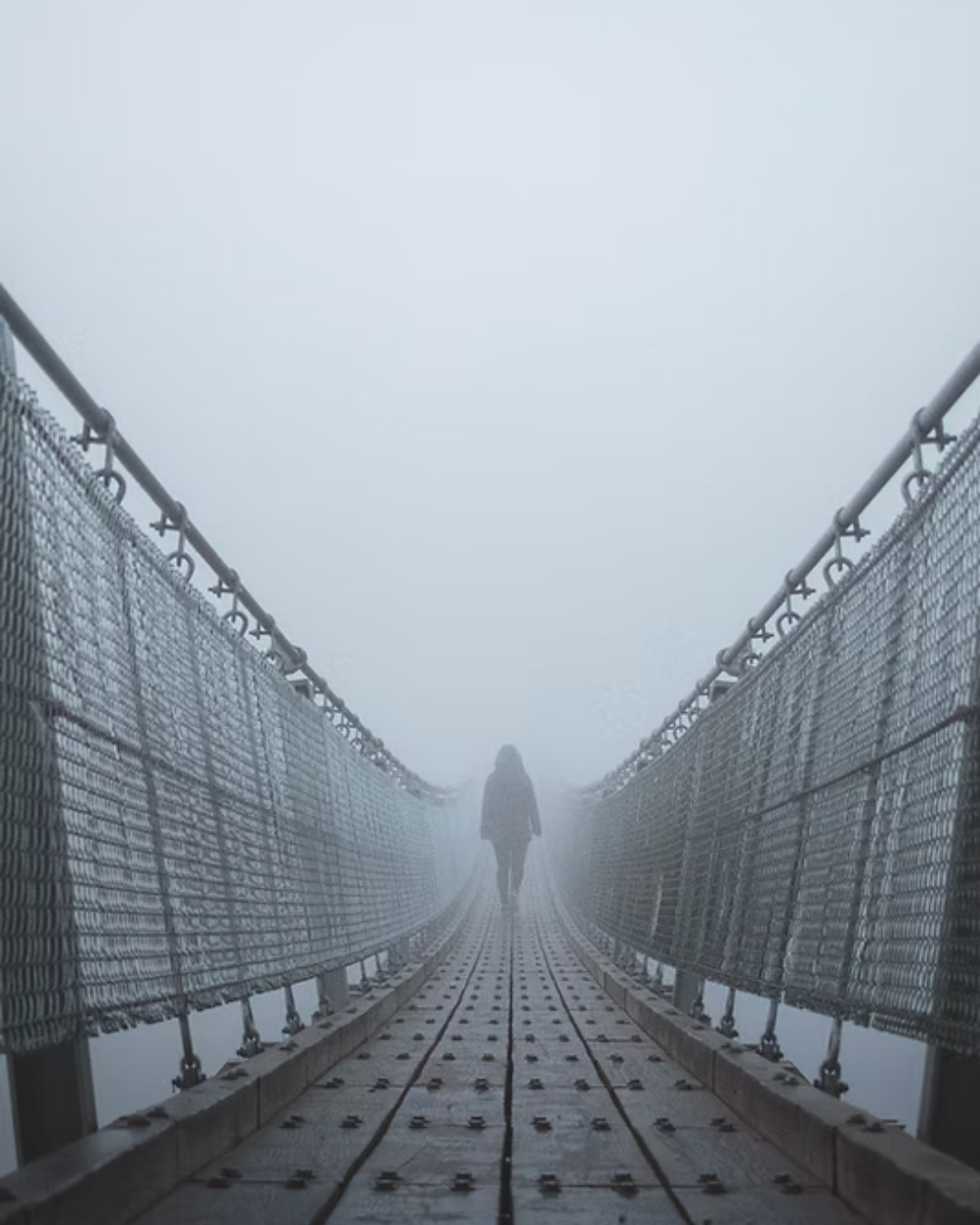 Person geht auf einer hölzernen Hängebrücke durch dichten Nebel.