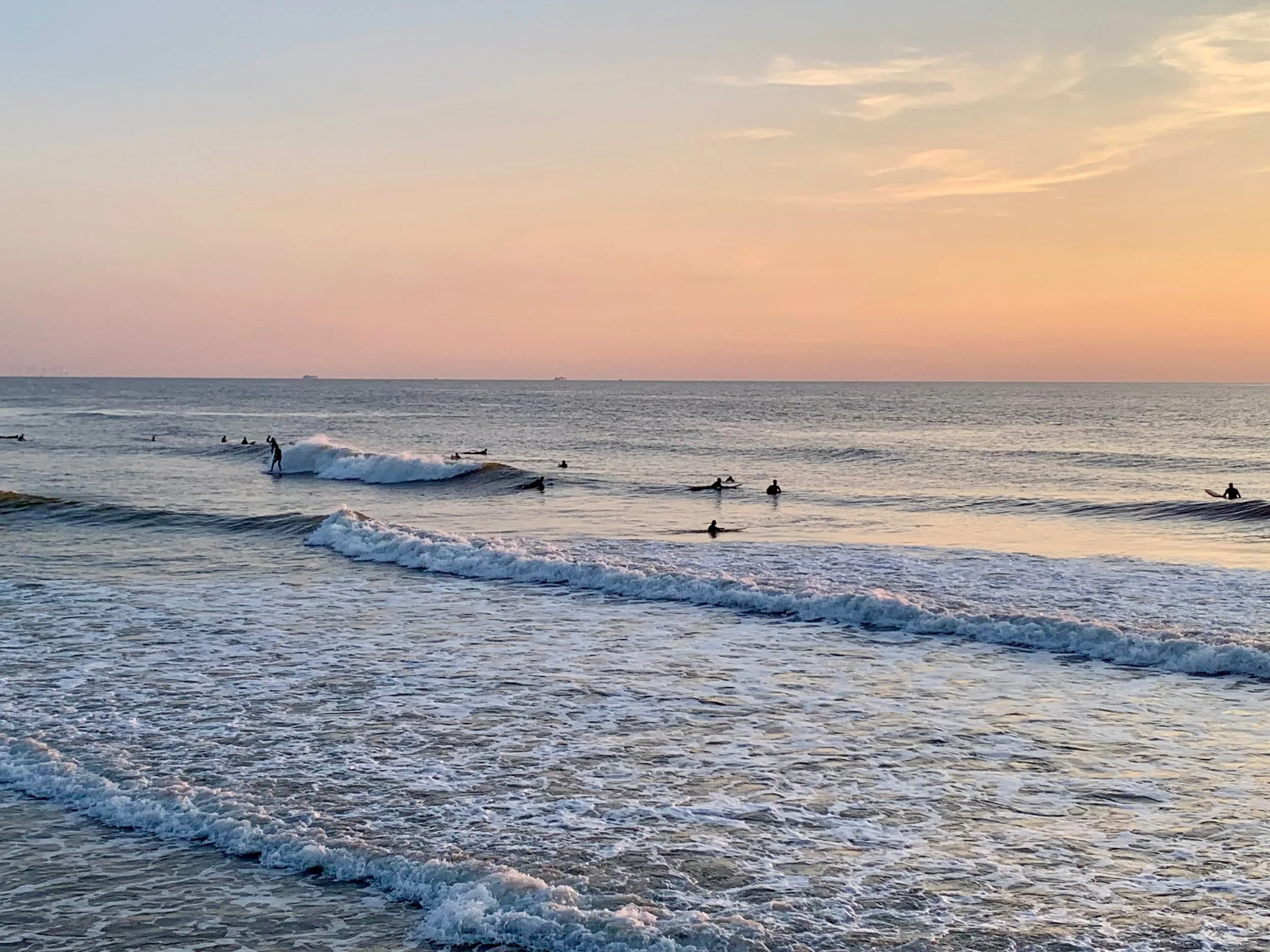A surfer riding a small breaking wave in golden evening light on the North Sea