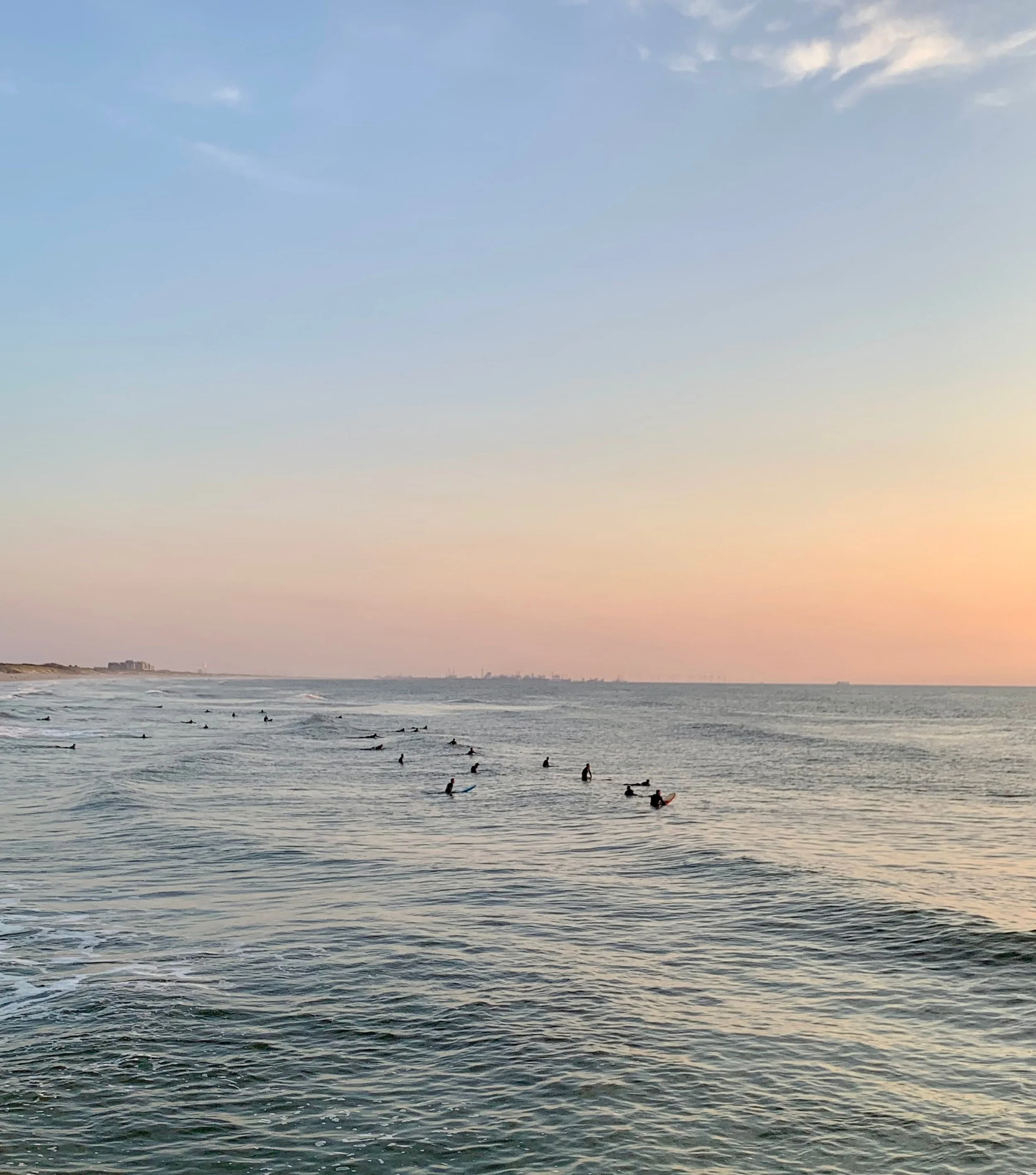 Surfers floating in the calm North Sea at dusk at Zuiderstrand, The Hague, with the coastline fading into the distance