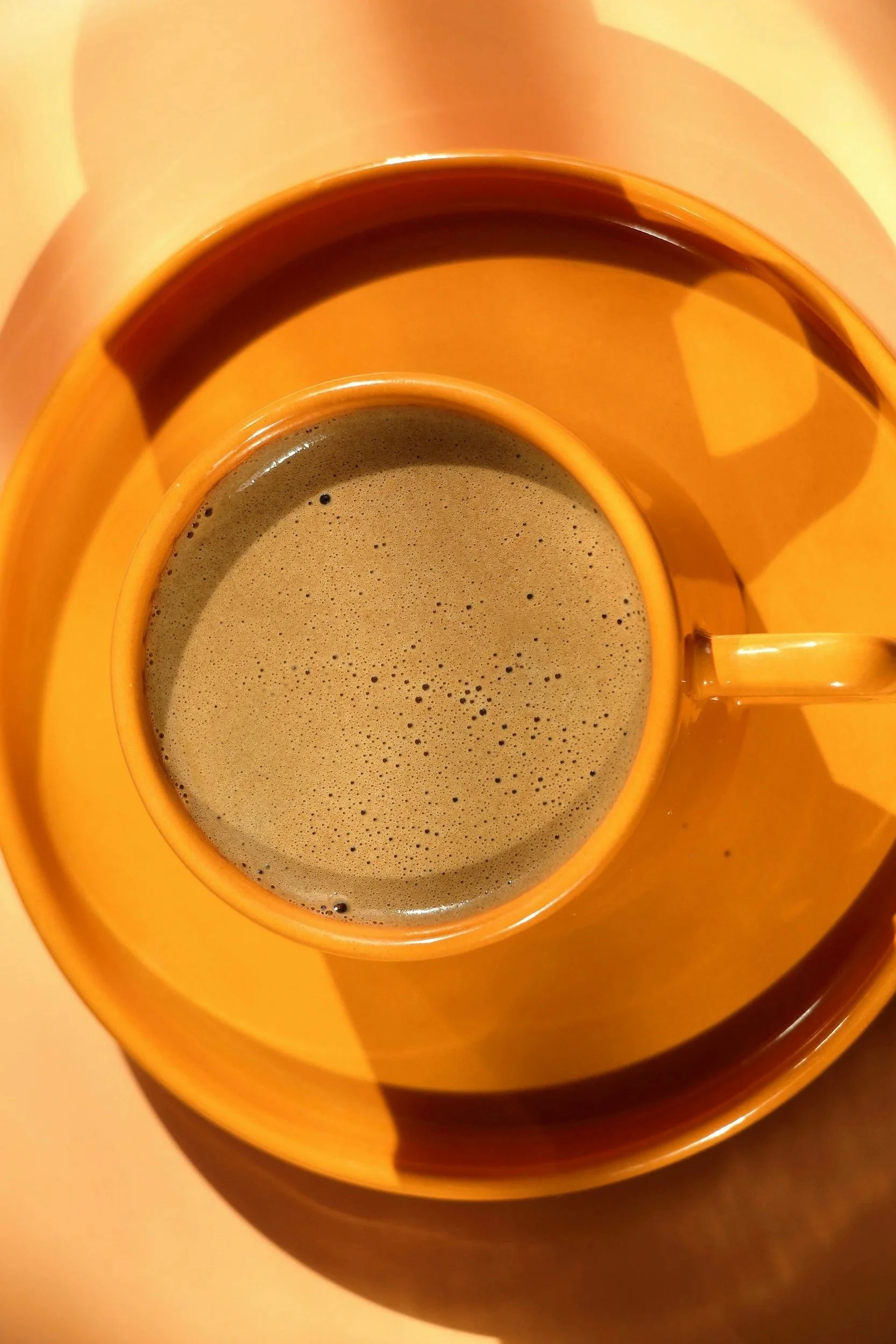 A close-up of a cup filled with coffee or a similar dark hot beverage inside a yellow saucer.