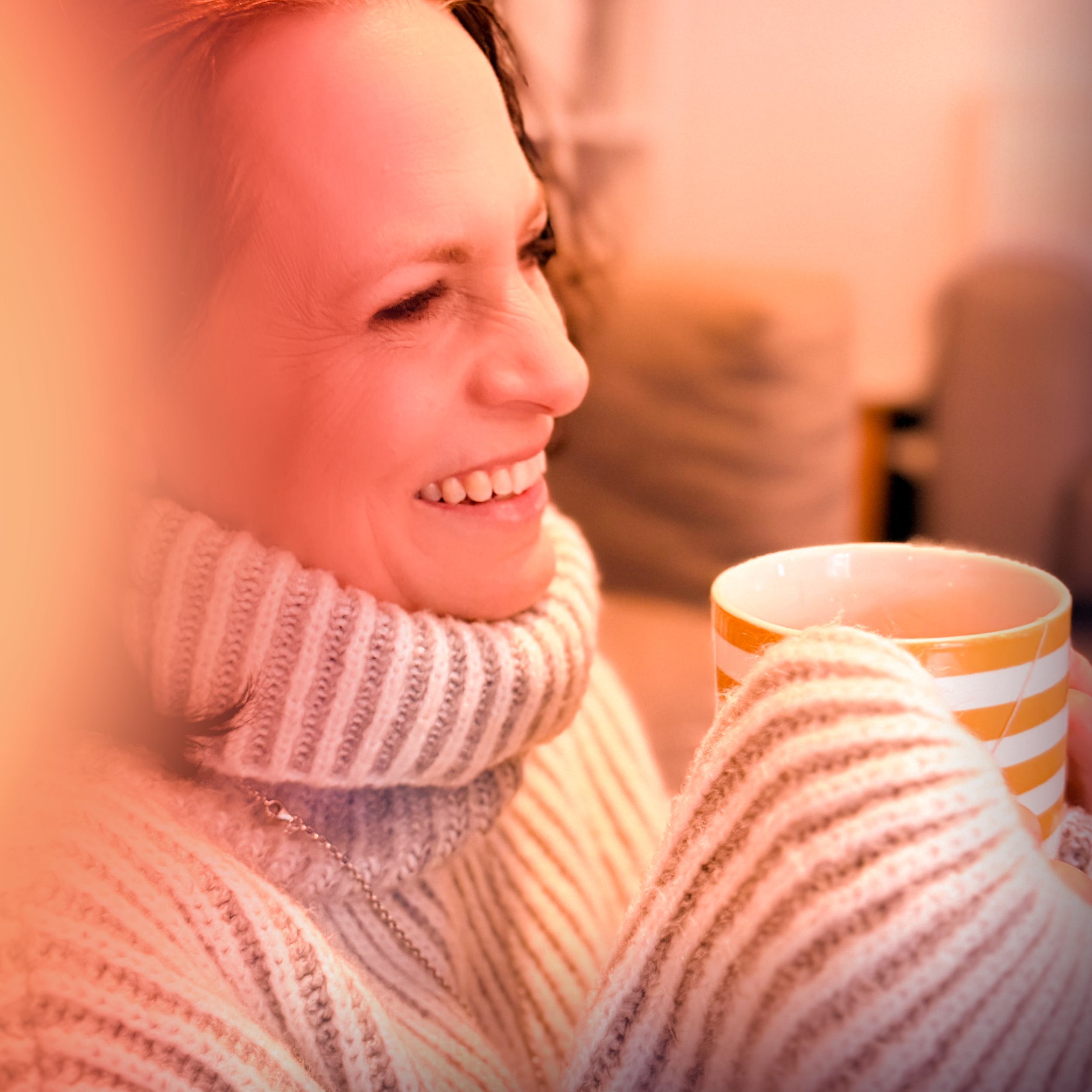 Close-up of a smiling young woman wearing a pink knitted sweater, holding a striped mug, with blurred background.