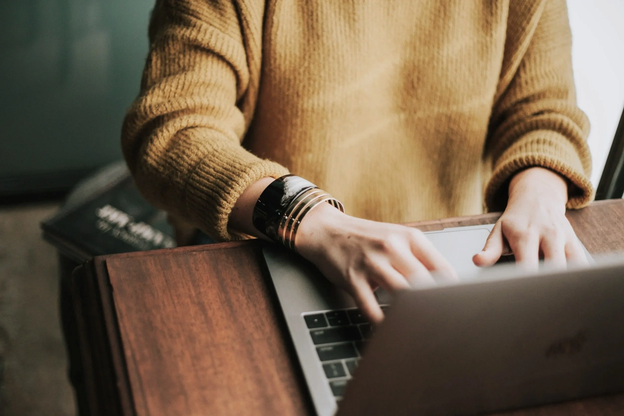 Person in a brown sweater using a laptop on a wooden desk.