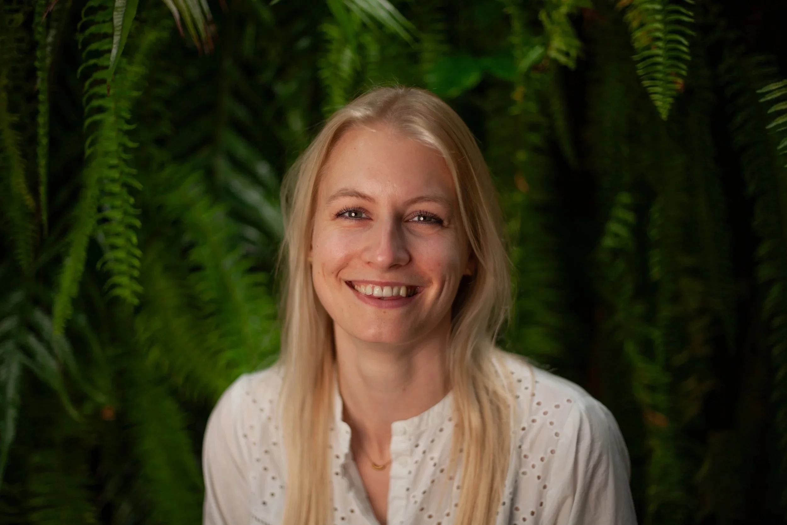 Profielfoto van een lachende blonde vrouw voor een groene achtergrond.