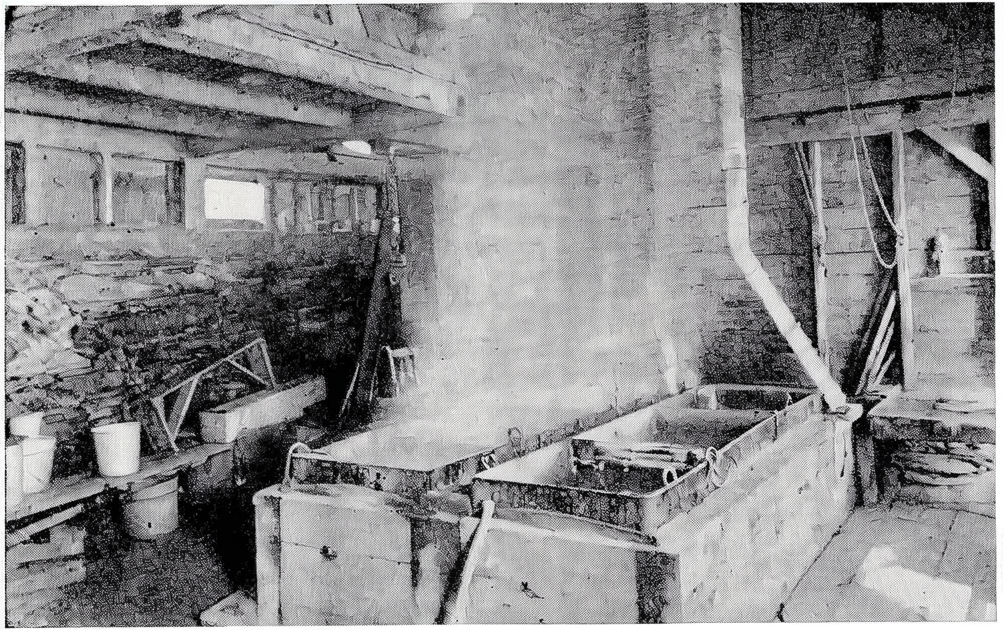 A vintage photo of a sugar hosue with wooden shelves, tables, and many evaporating trays and tools.