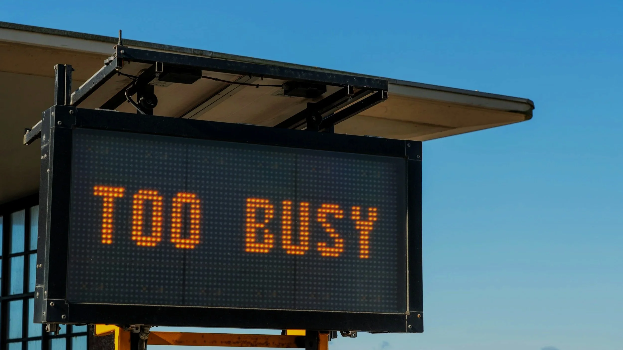 Electronic bus stop sign displaying message '100 BUS' against a clear blue sky.