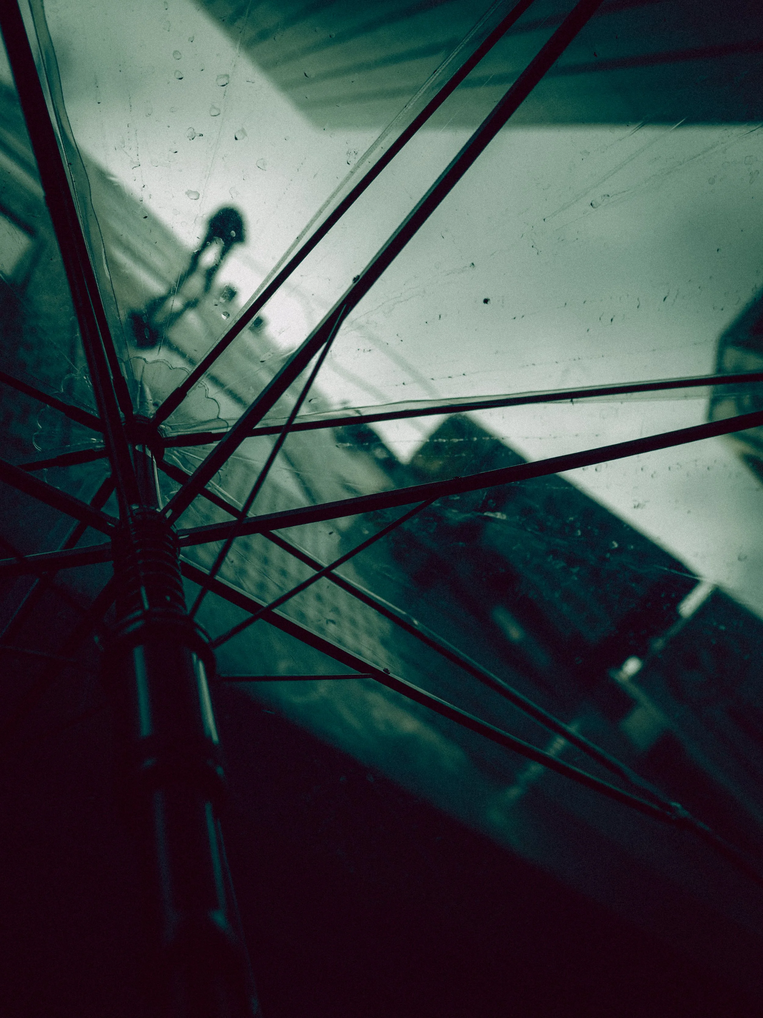 Looking up through an umbrela from underneath, dark clouds or sky in the background whilst a window cleaner scales down the side of the building