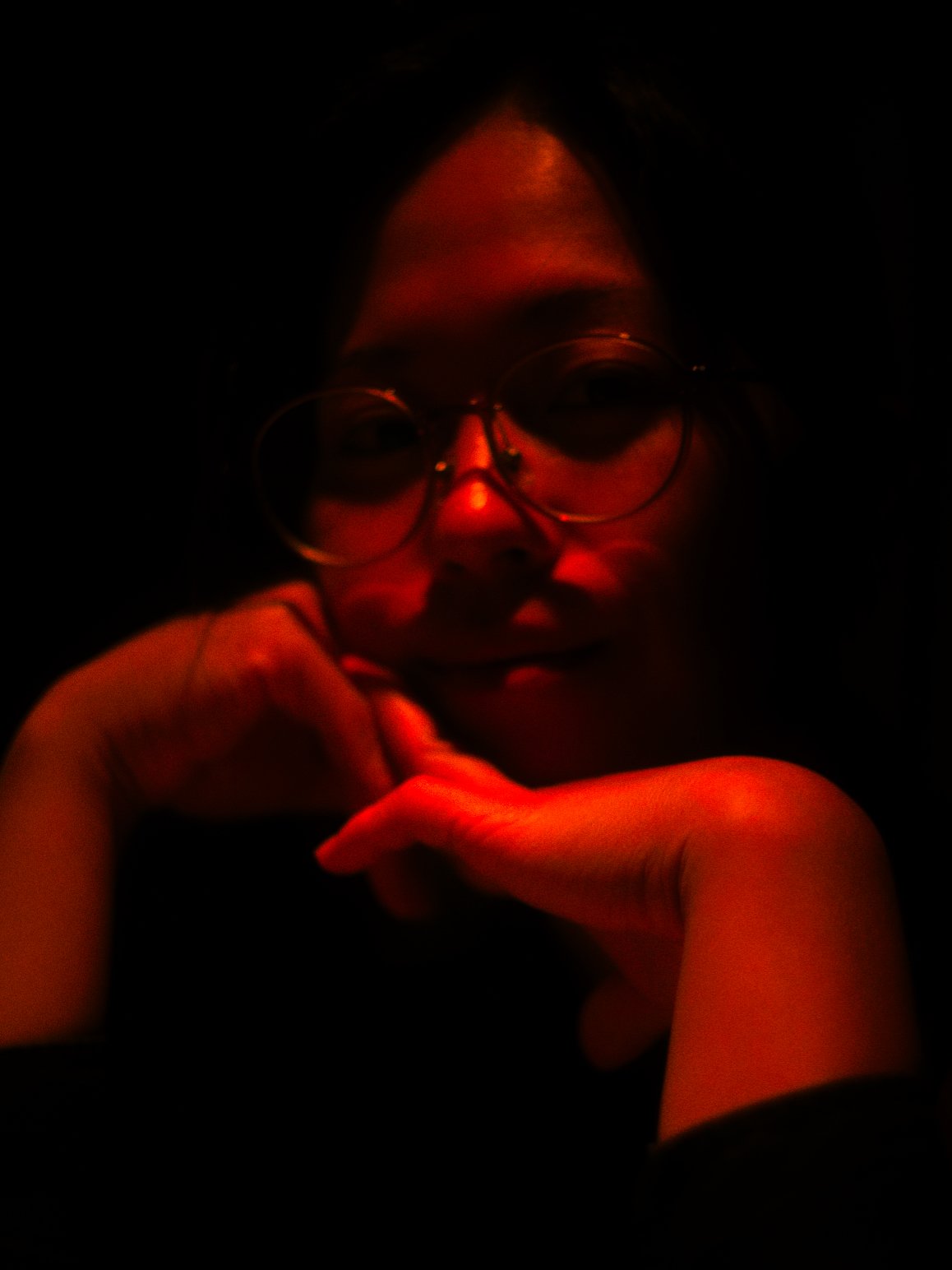 A person with glasses holding their chin in a dark environment with red lighting.