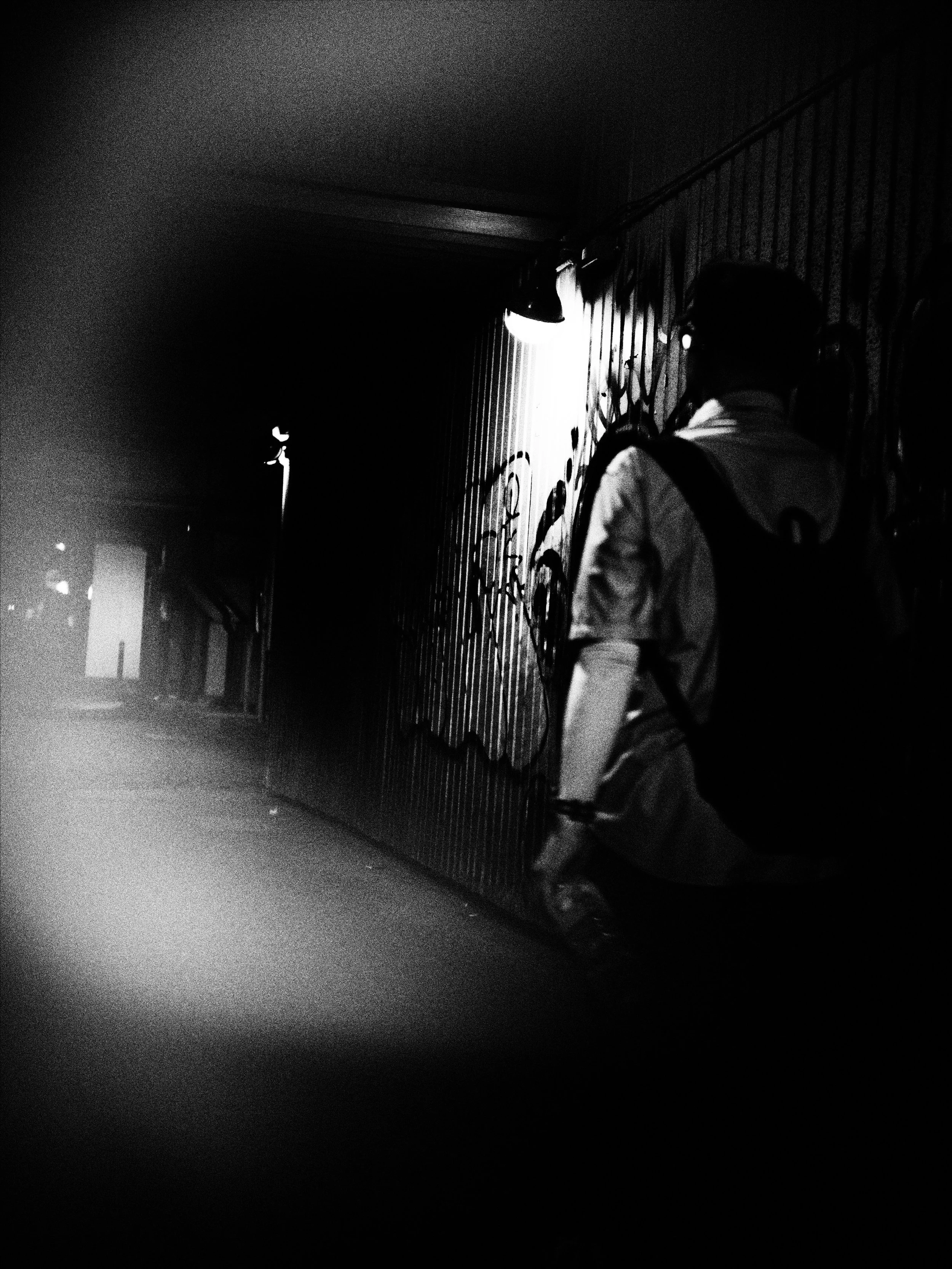 A person with pigtails and glasses sitting against a graffiti-covered wall at night, partially illuminated by a streetlight.