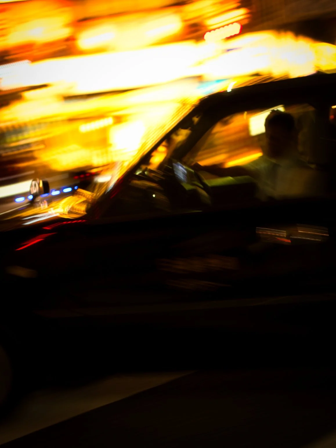 Blurred motion photo of a person driving a car at night with bright city lights in the background.