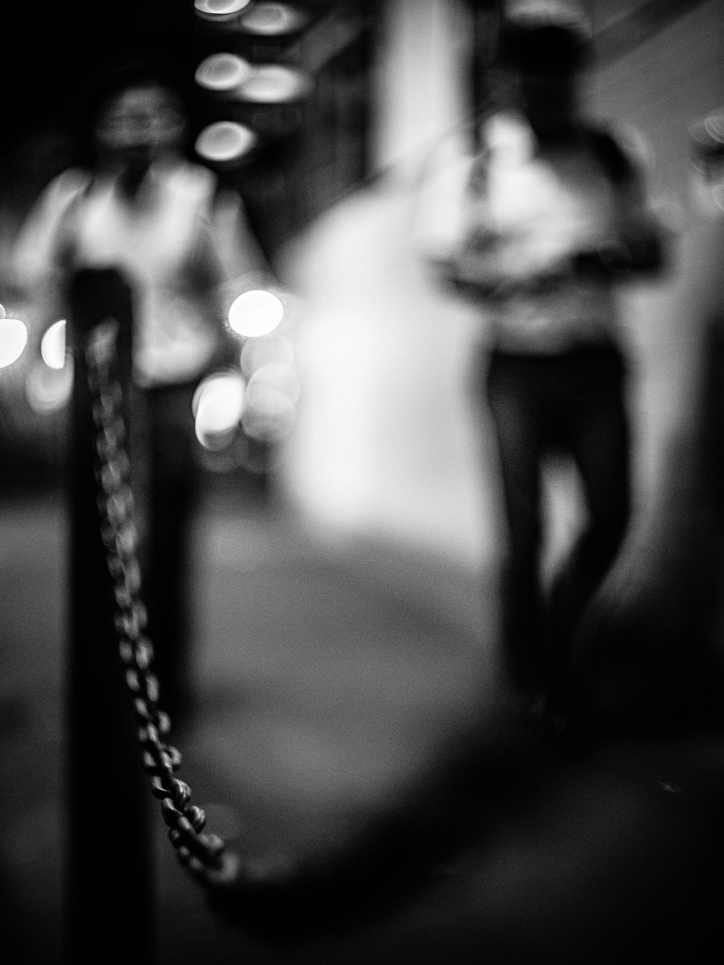 Blurred black and white photo of a person's lips, with a chain to their left side and a cable or wire in front.