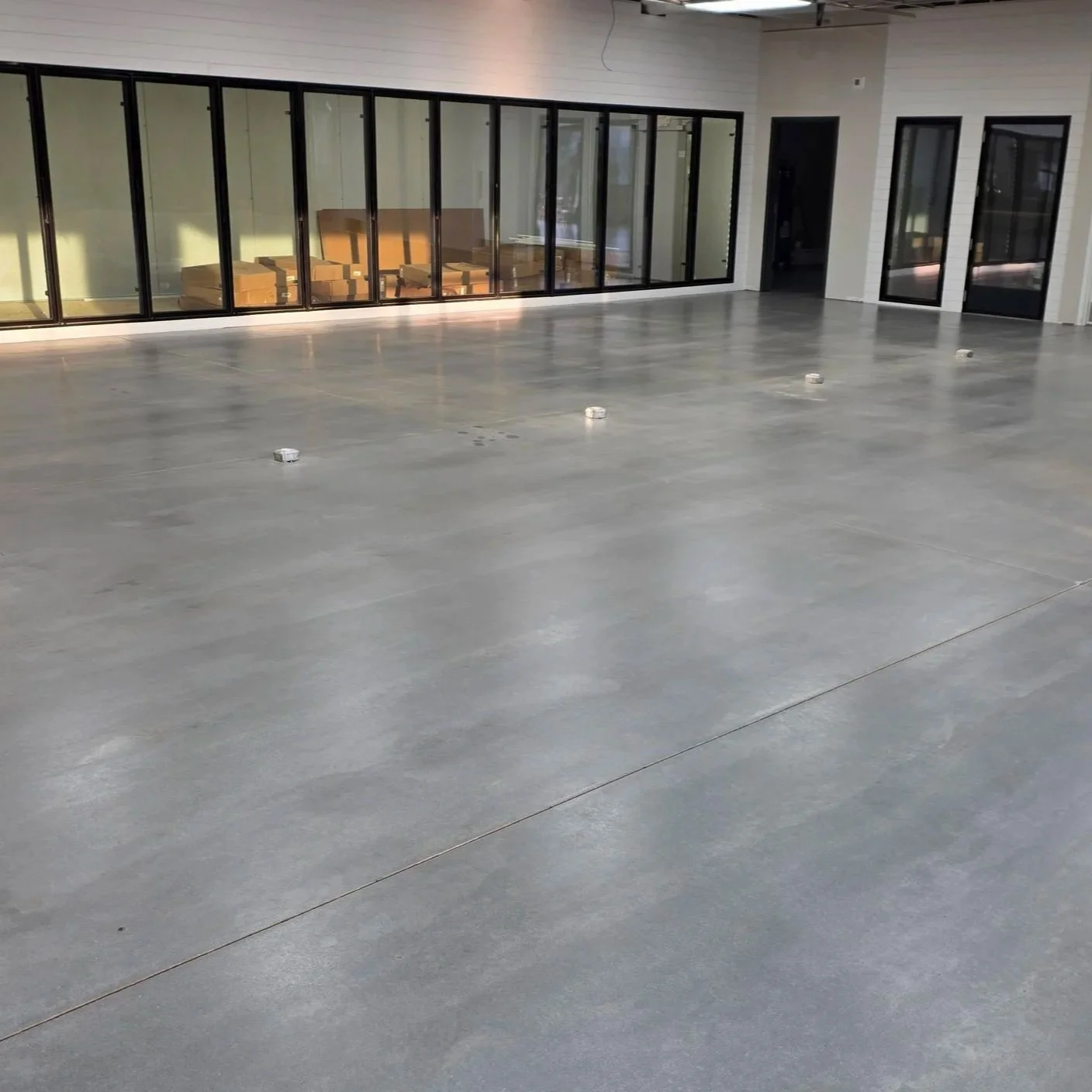 An empty commercial space with polished concrete floors, large glass windows, and a door, ready for setup or renovation.