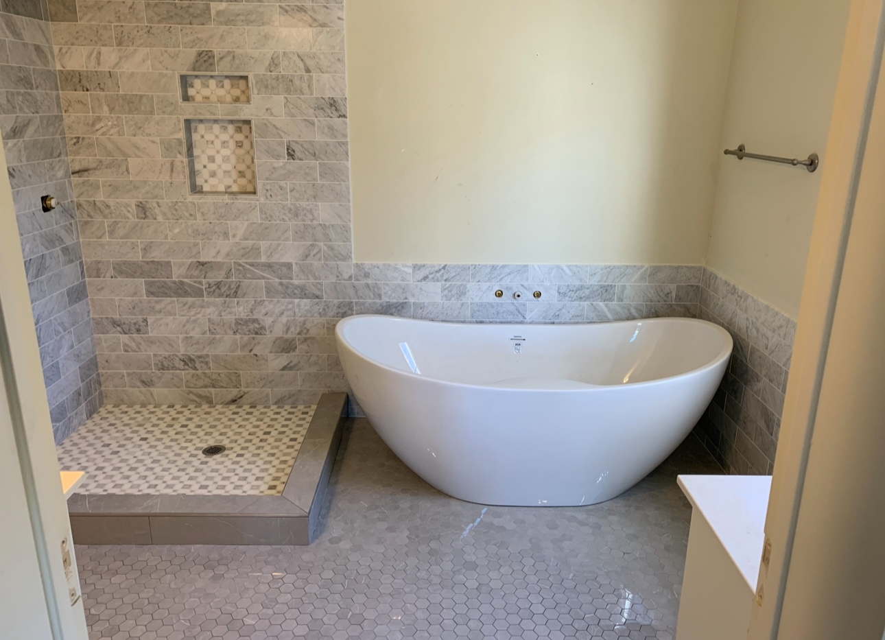 Modern bathroom with a freestanding bathtub, a walk-in shower area with grey tiled walls and a small niche, and a hexagonal tile floor.
