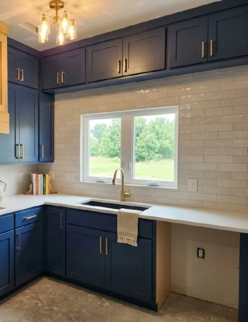 Kitchen with blue cabinets, white countertop, and a window above the sink showing green trees outdoors.