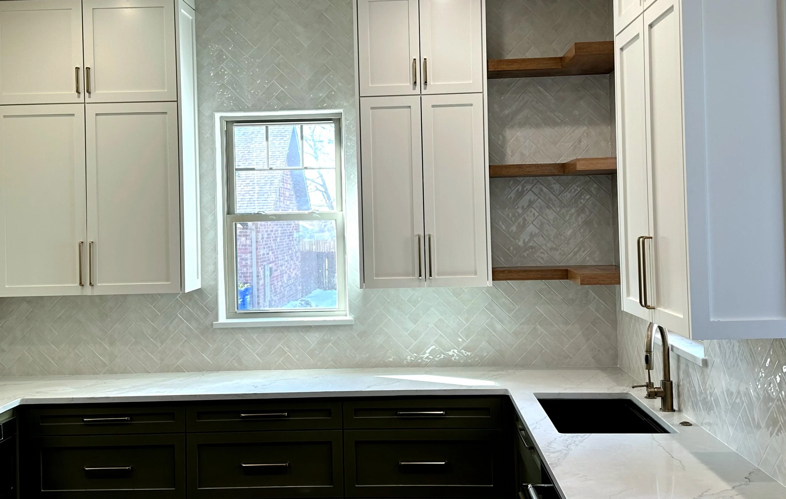 Modern kitchen with white cabinets, wood open shelves, a window with a view of a brick house and roof, a marble countertop, and a modern faucet.