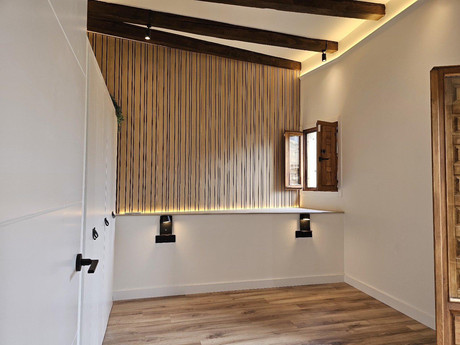 Reforma integral de dormitorio con panel decorativo de madera, iluminación LED indirecta y acabados personalizados realizada por Reformas Barna Decor.