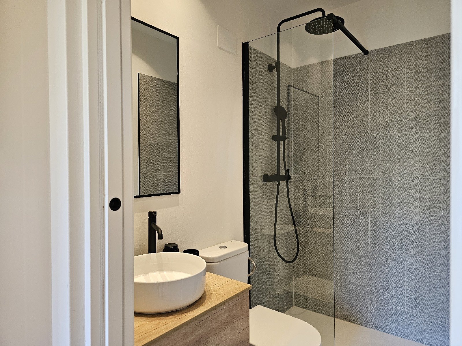 Reforma integral de baño con ducha de obra, mampara de vidrio, revestimientos porcelánicos y grifería en acabado negro realizada en Barcelo