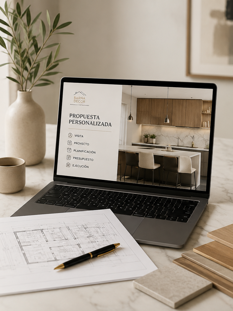 A laptop displaying a website for a home decor business with a modern kitchen on the screen, a blueprint with a pen, a potted plant, and some material samples on a marble table.