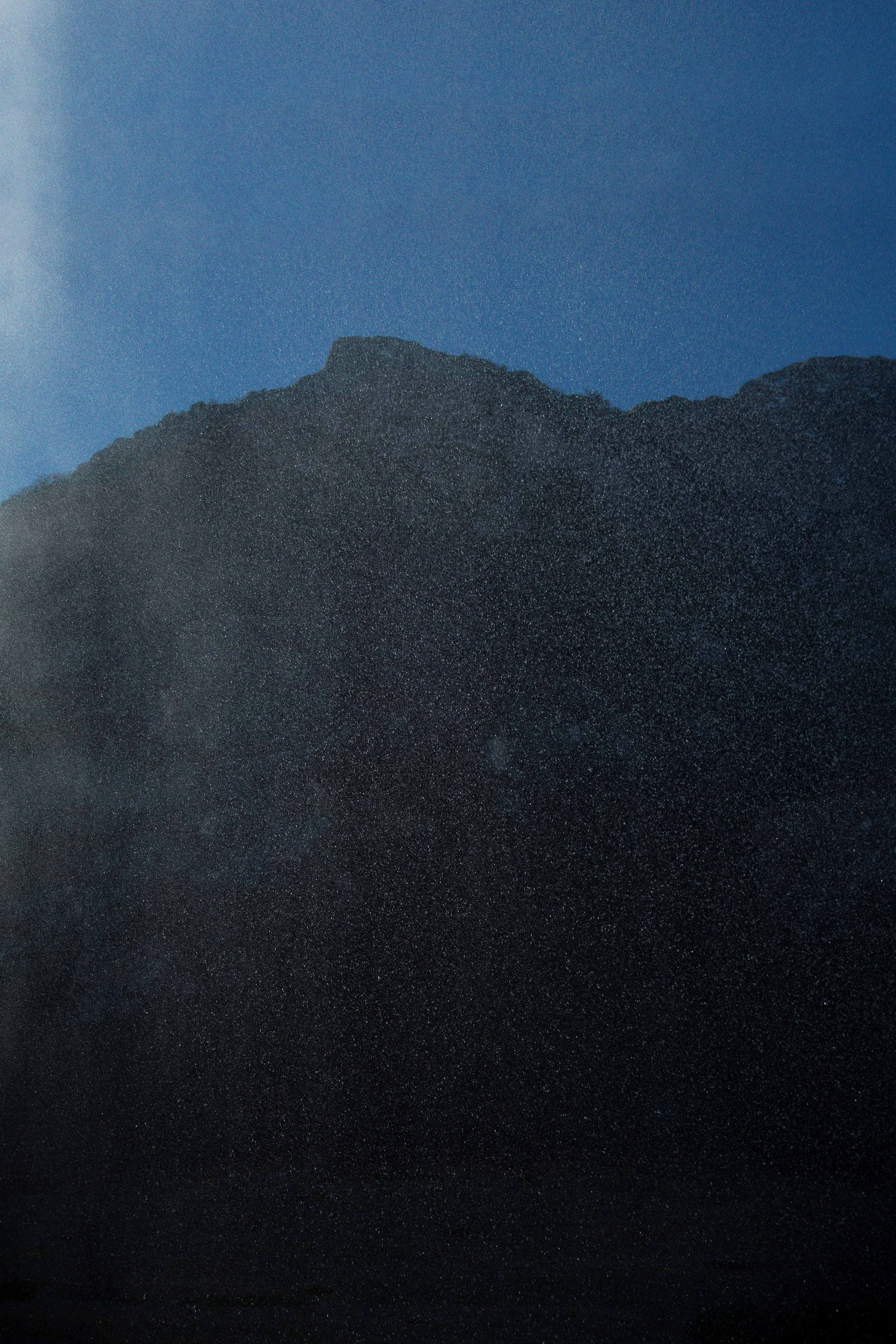 Nighttime mountain landscape with starry sky and a faint glow on the horizon.