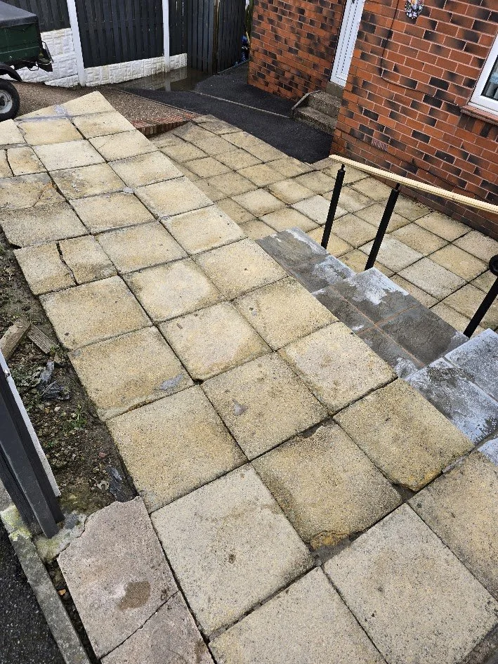 Newly paved concrete or stone steps leading up to a brick house with brick and white siding, featuring a handrail on right side, outside a residential building.