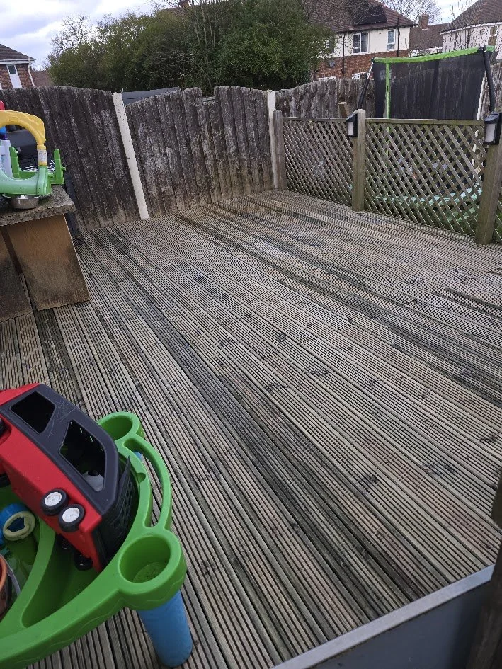 A backyard wooden deck with a picket fence and a lattice gate, scattered toys including a toy truck and a plastic playset.