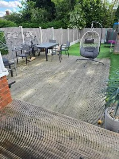 Backyard patio with outdoor furniture and a hanging egg chair, fenced yard with trees and plants.