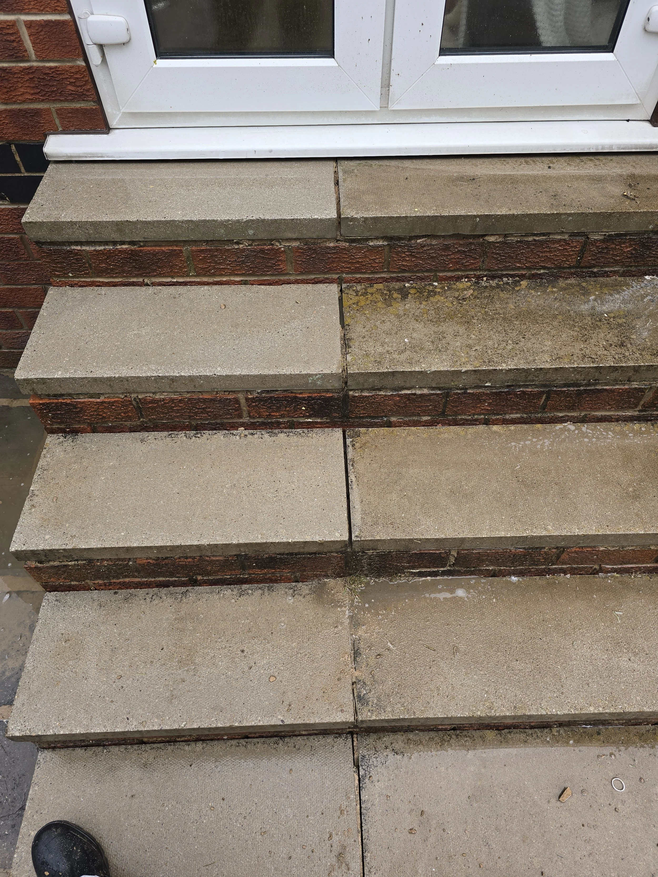 Concrete steps leading up to a glass door with a white frame, attached to a brick wall. The steps are dirty and weathered.
