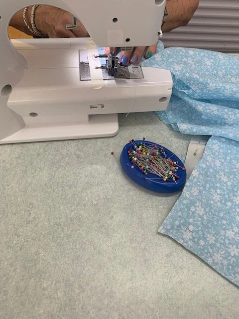 A person sewing fabric on a sewing machine with a pin cushion and floral fabric nearby.