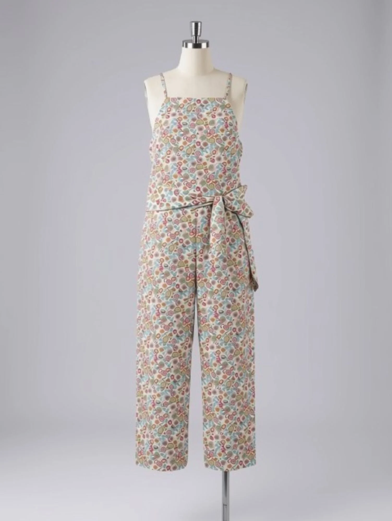 A mannequin displays a sleeveless, floral-patterned, light-colored jumpsuit with a tied waist.