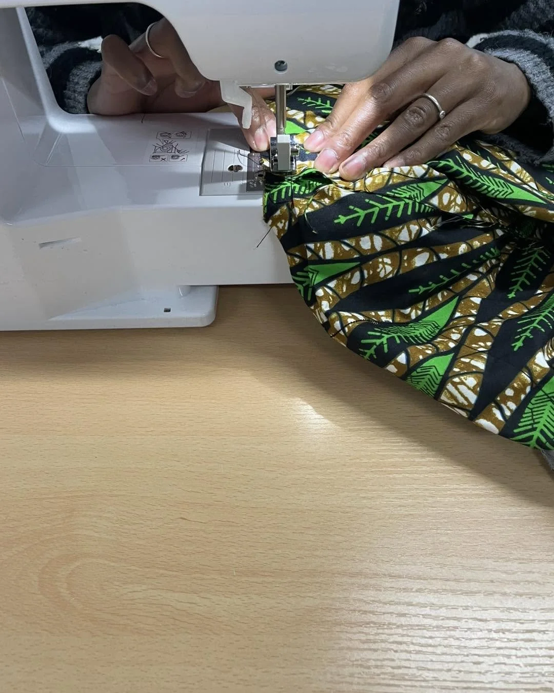 Person sewing colorful patterned fabric on a white sewing machine on a wooden table.