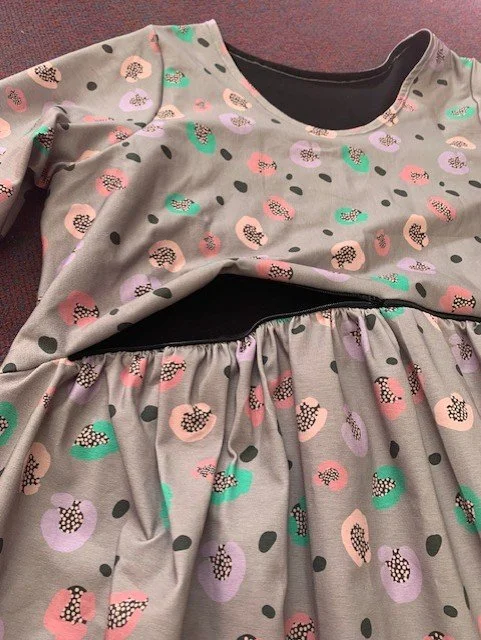 A dress with a grey background featuring pastel-colored grapes and black dots, laid flat on a surface.