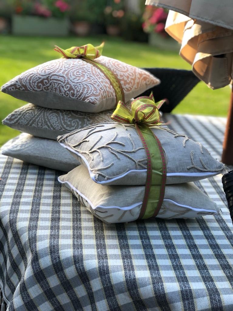 Four decorative throw pillows stacked on top of each other on a checkered tablecloth outdoors, with ribbons tied around the pillows.