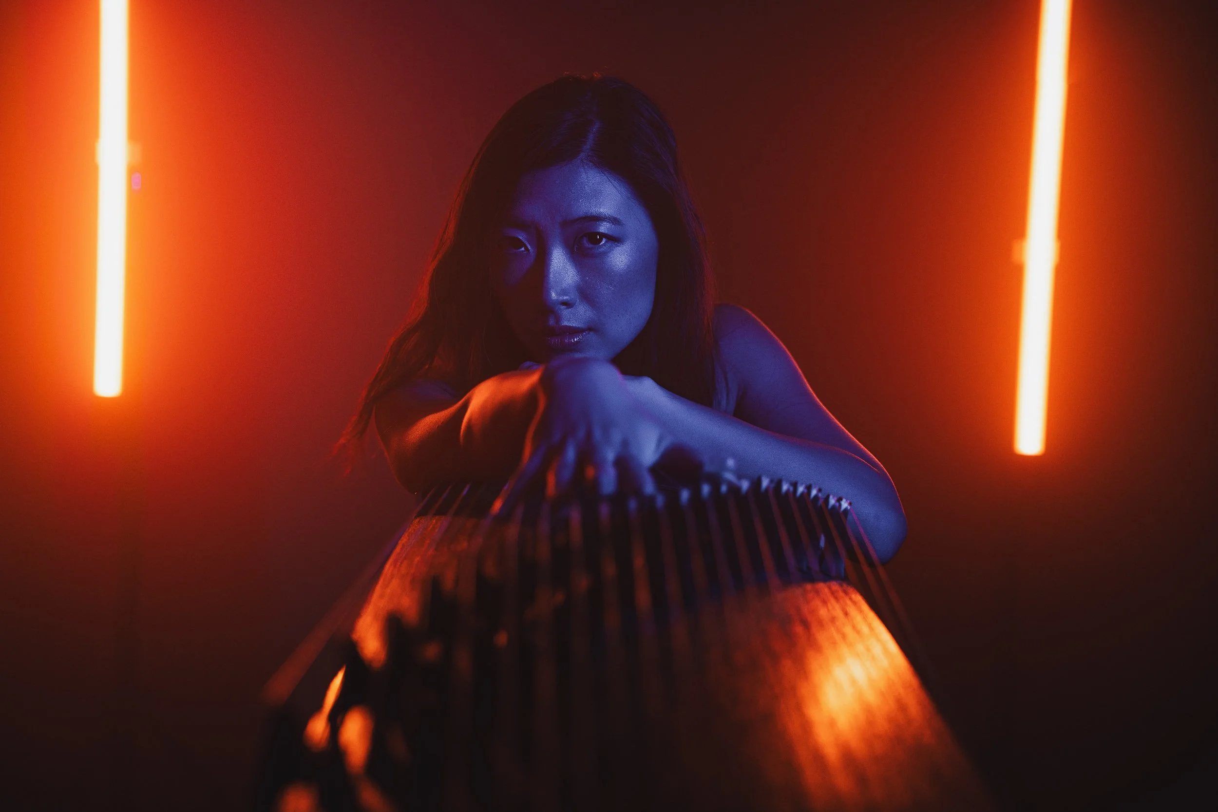 A woman with long hair leaning on a wooden surface, illuminated by vertical pink neon lights in a dark room with red and purple lighting.