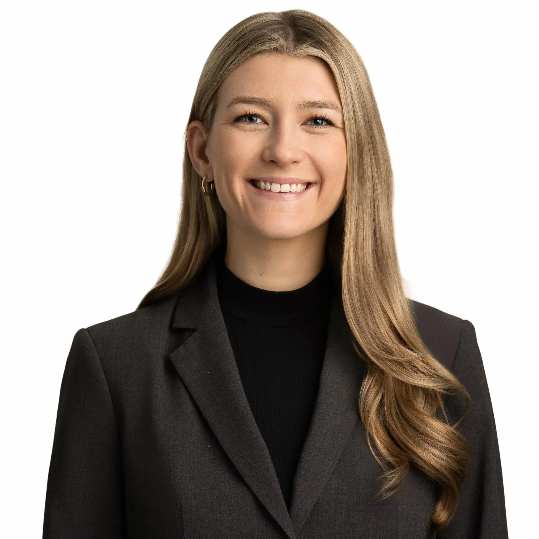 A professional portrait of a smiling woman with long blonde hair, wearing a black turtleneck and a dark blazer, against a white background.