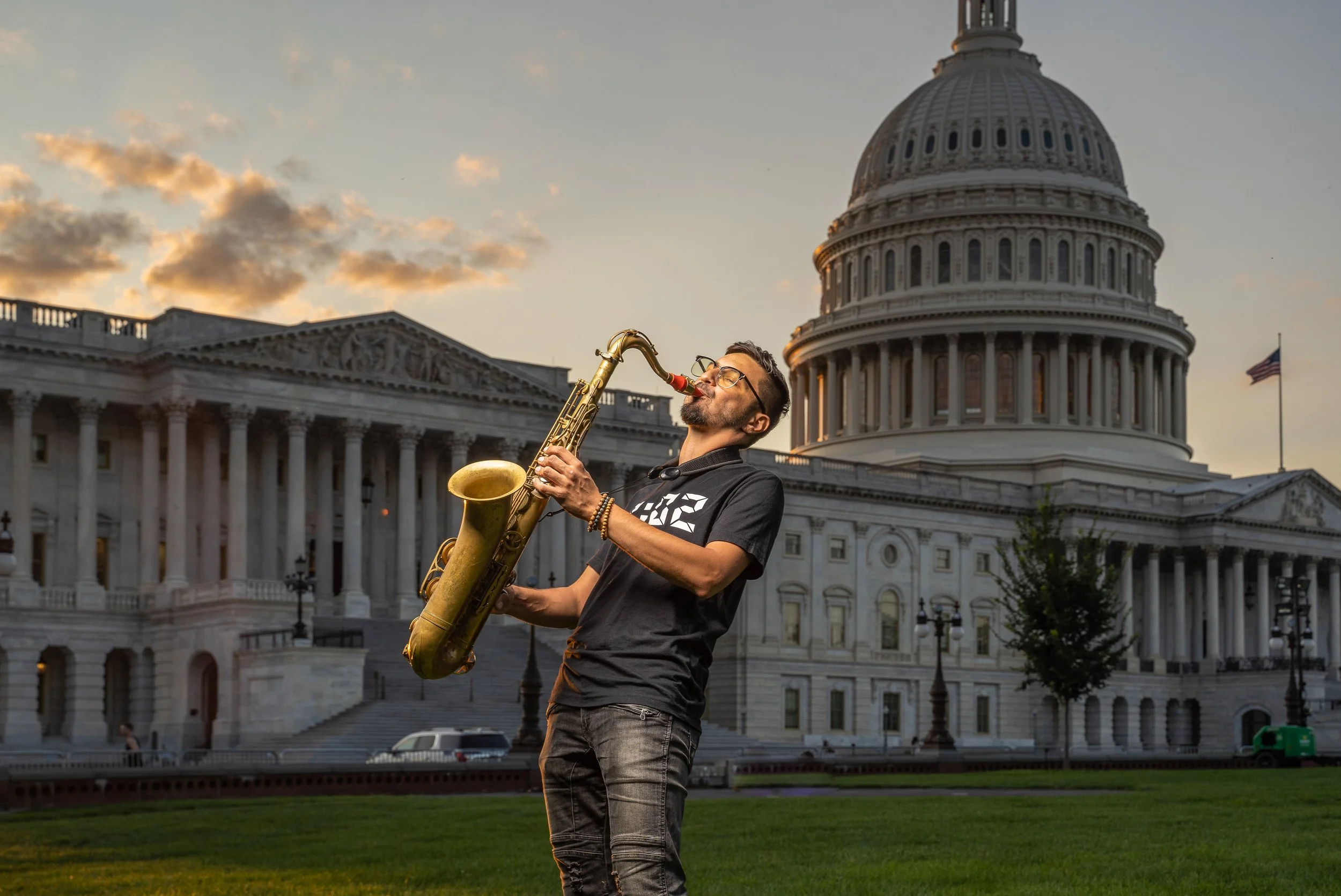Man playing saxophone in front of the U.S. Capitol building during sunset.
