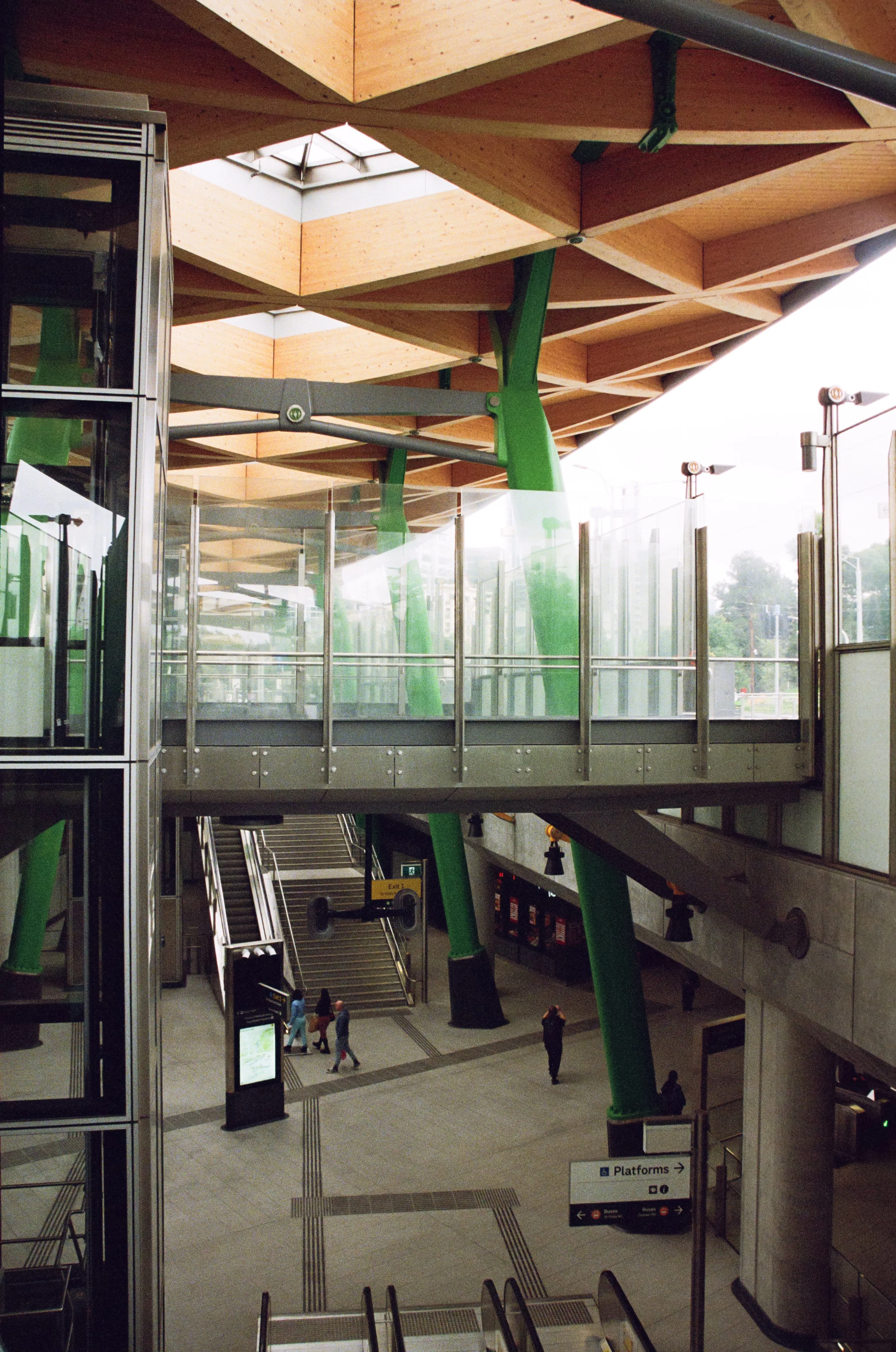 Interior of Anzac Station in Melbourne. Metro train station with escalators, stairs, and a spacious walkway. Architectural platforms and signage are visible, and a few people are walking through the area.
