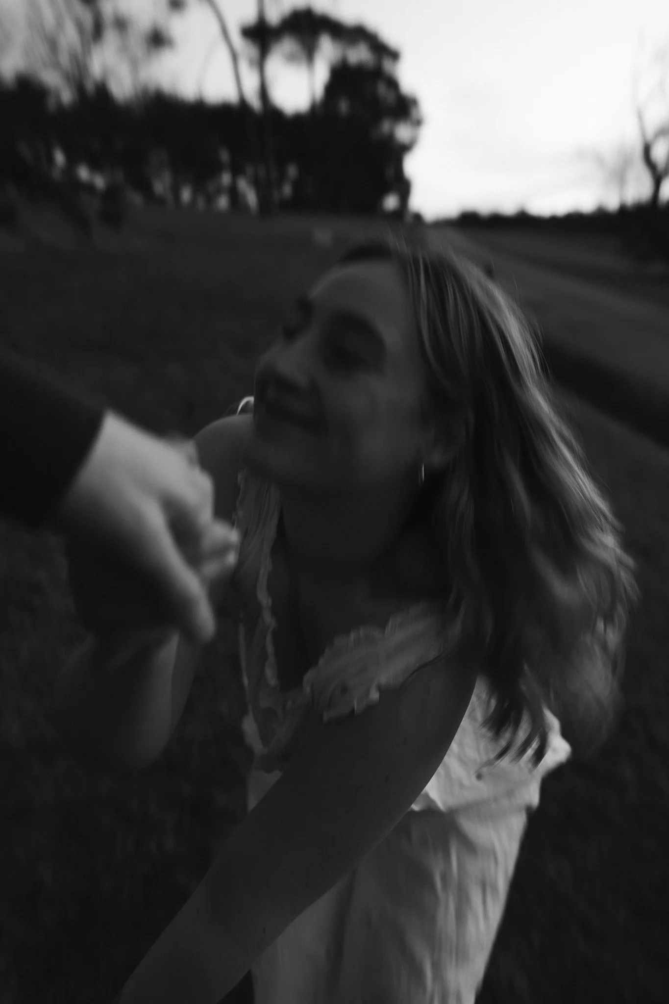 A person holding hands, with both in focus in black and white, outdoors with trees and a house in the background.
