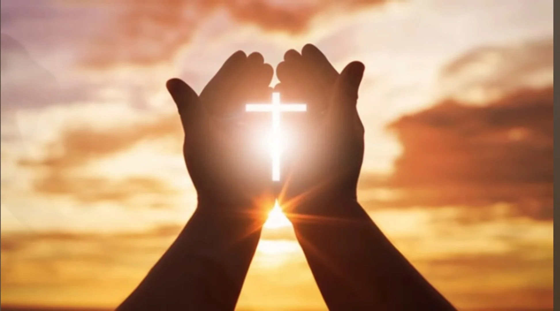 A silhouette of hands forming a heart shape with the sun shining through the gap, set against a vibrant sunset sky with clouds.
