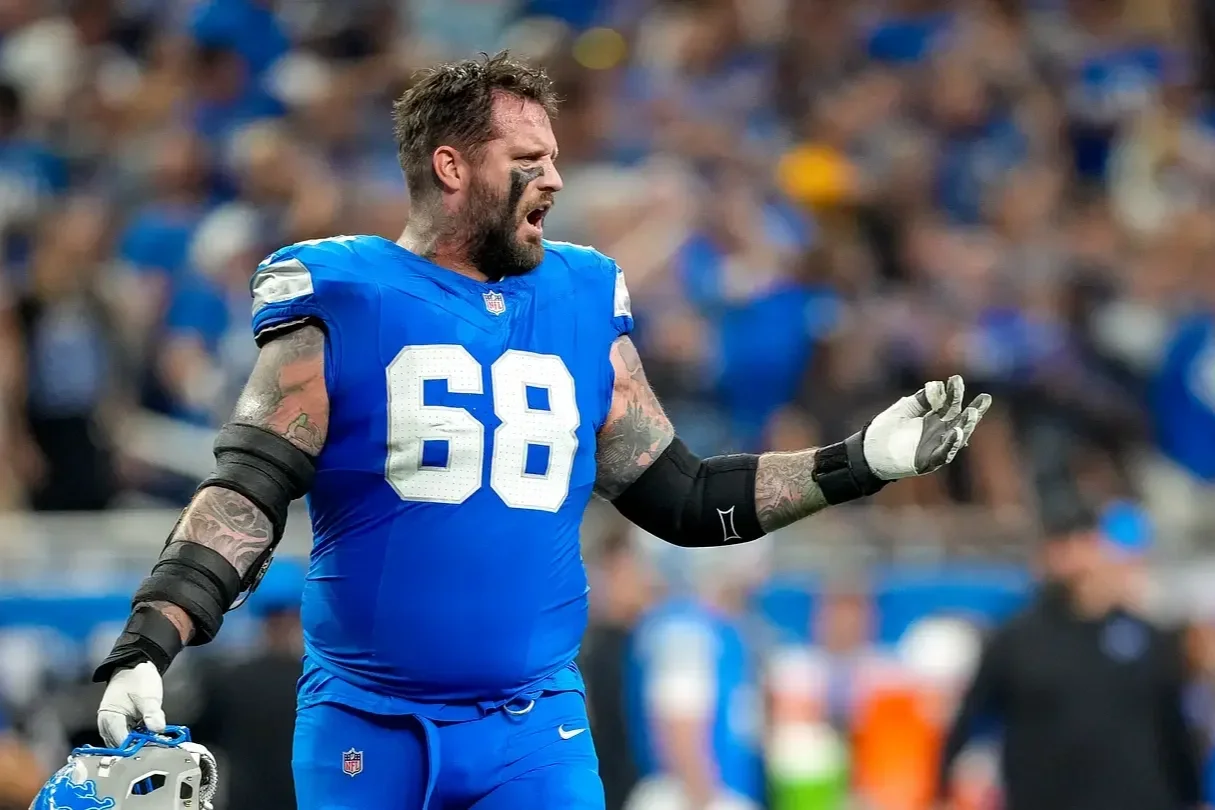 NFL player wearing a blue jersey with the number 68, black arm pads, and a white glove, holding a helmet, on a football field during a game.