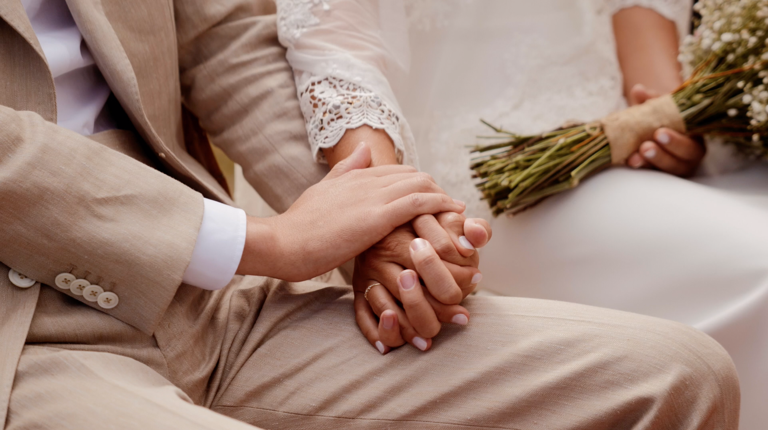 Close-up of a couple holding hands during their wedding ceremony, with the bride holding a bouquet of flowers.