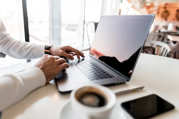 Person working on a laptop at a white table, with a coffee cup and a smartphone nearby.