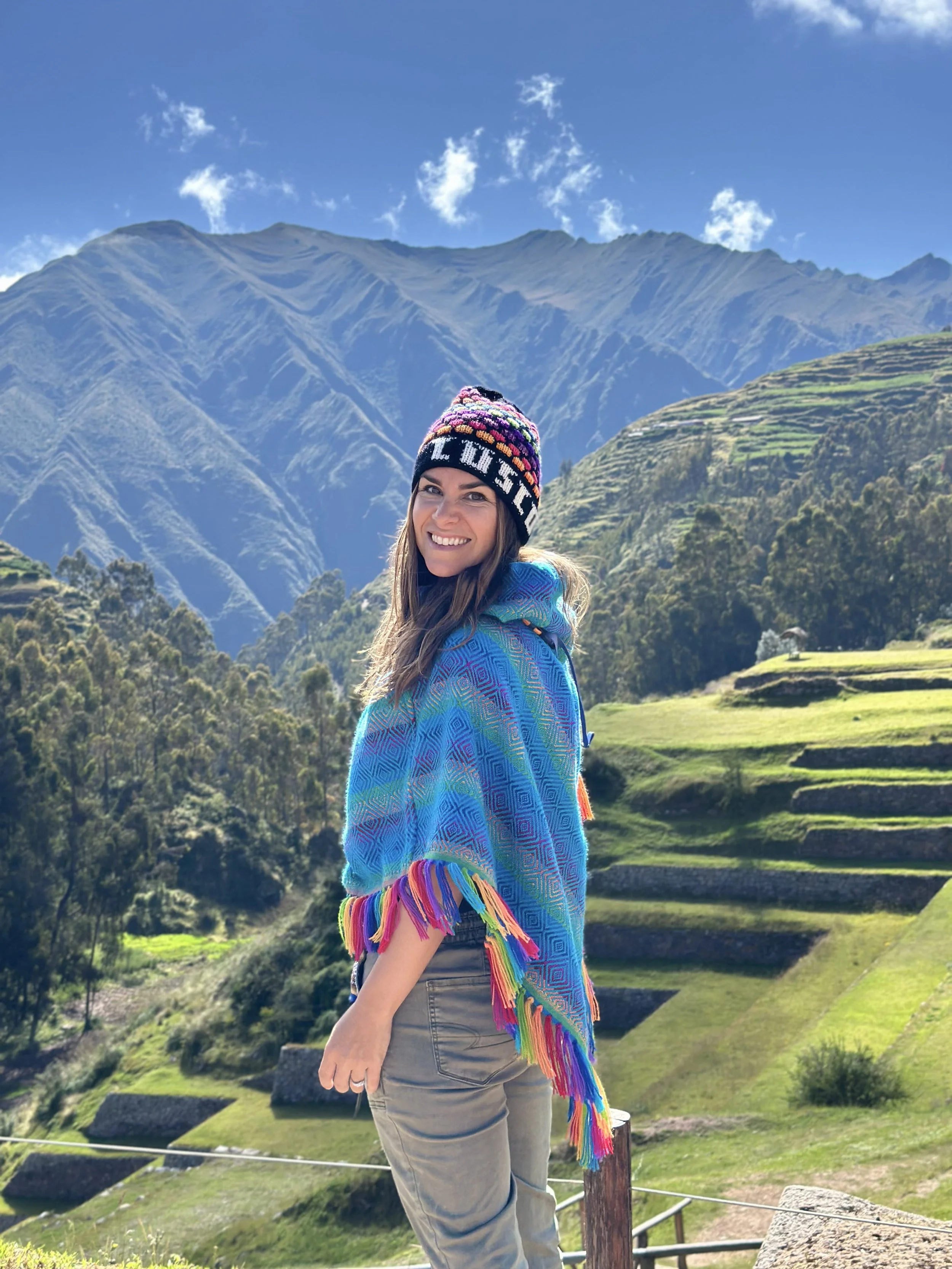 Femme souriante portant un chapeau coloré dans un paysage de montagnes vertes et de terrasses agricoles en terrasses.