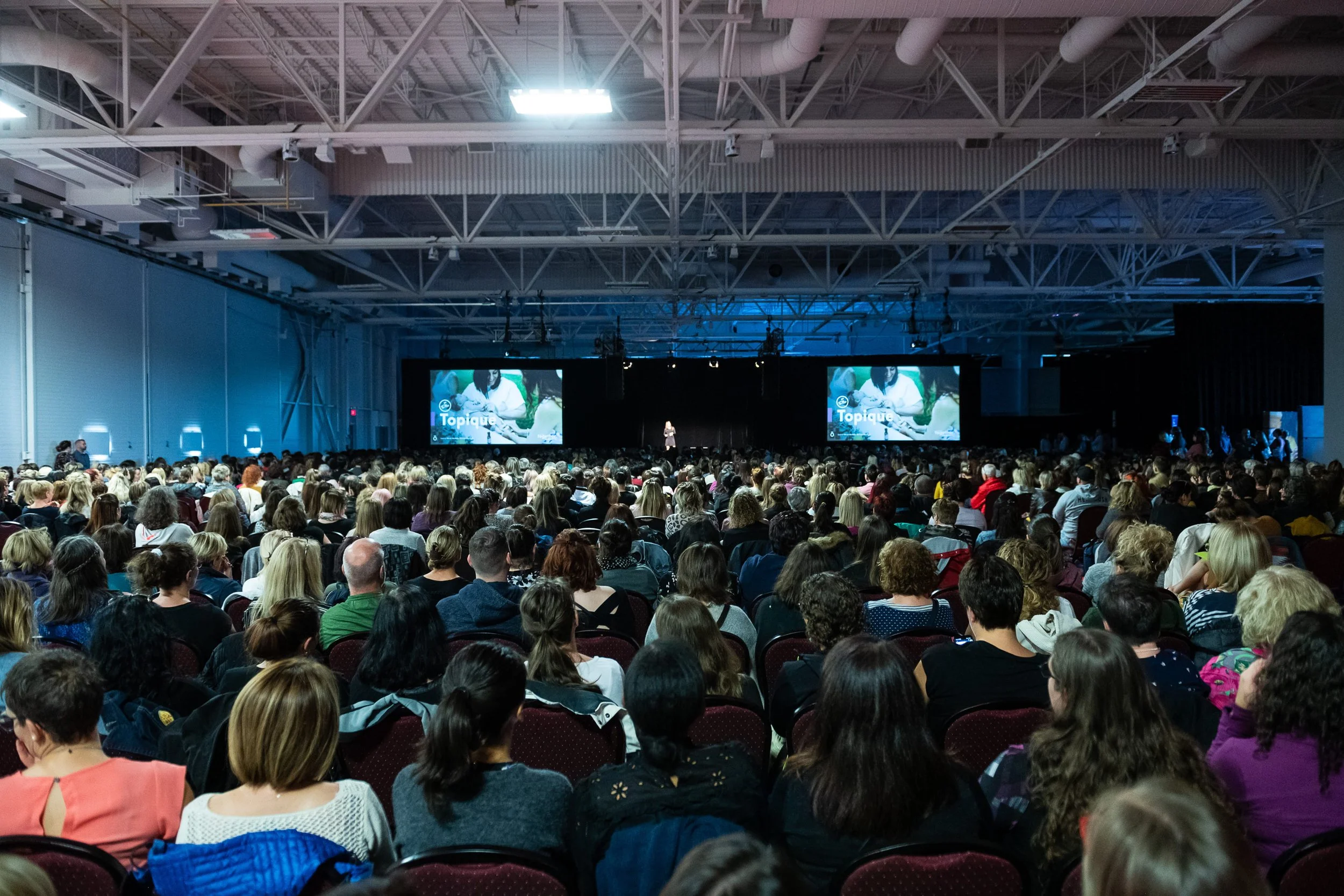 Une grande audience assise dans une salle d'événement regardant un écran avec une présentation.
