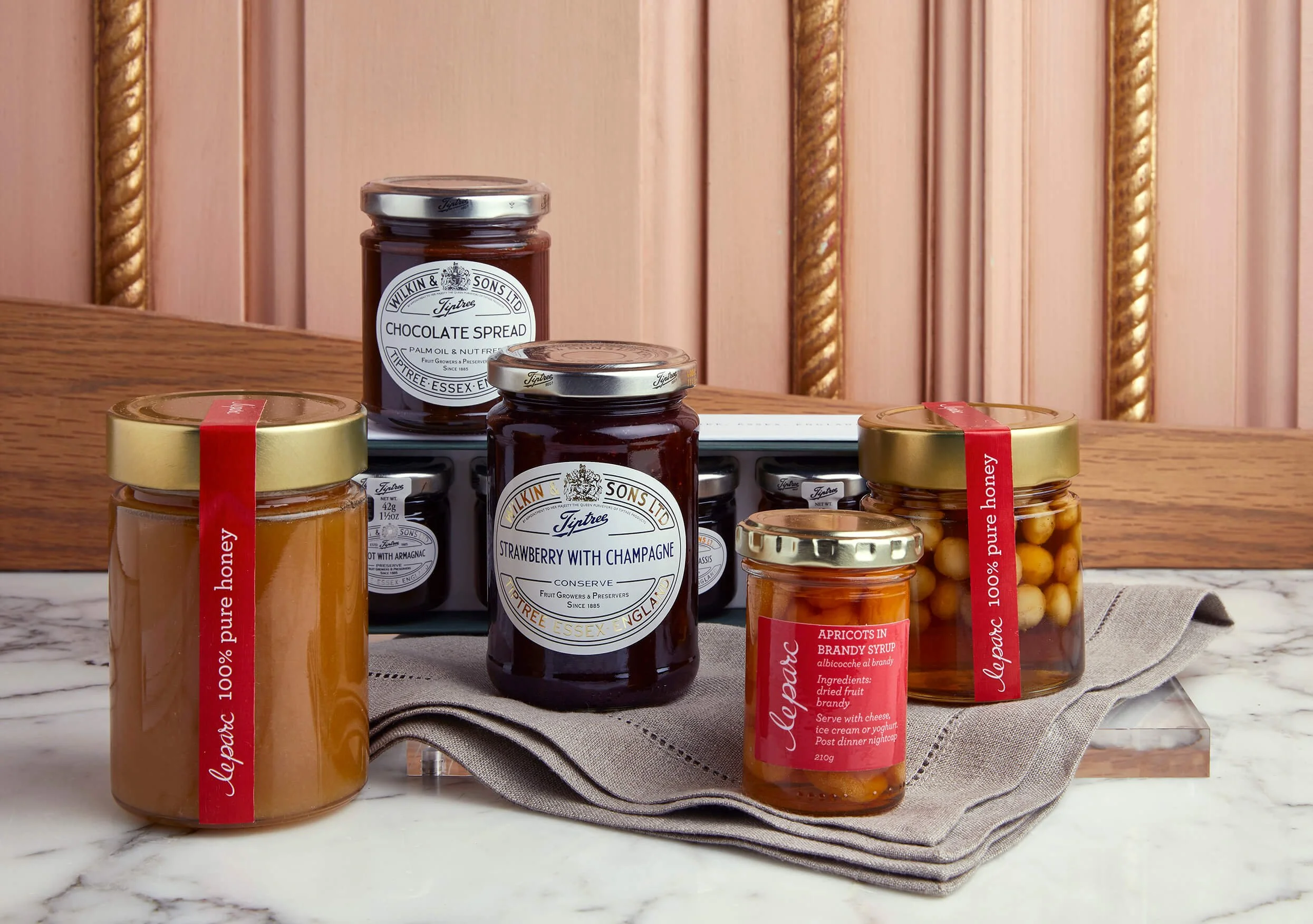 Several jars of homemade preserves and jams on a table with a cloth, with a wooden panel background.