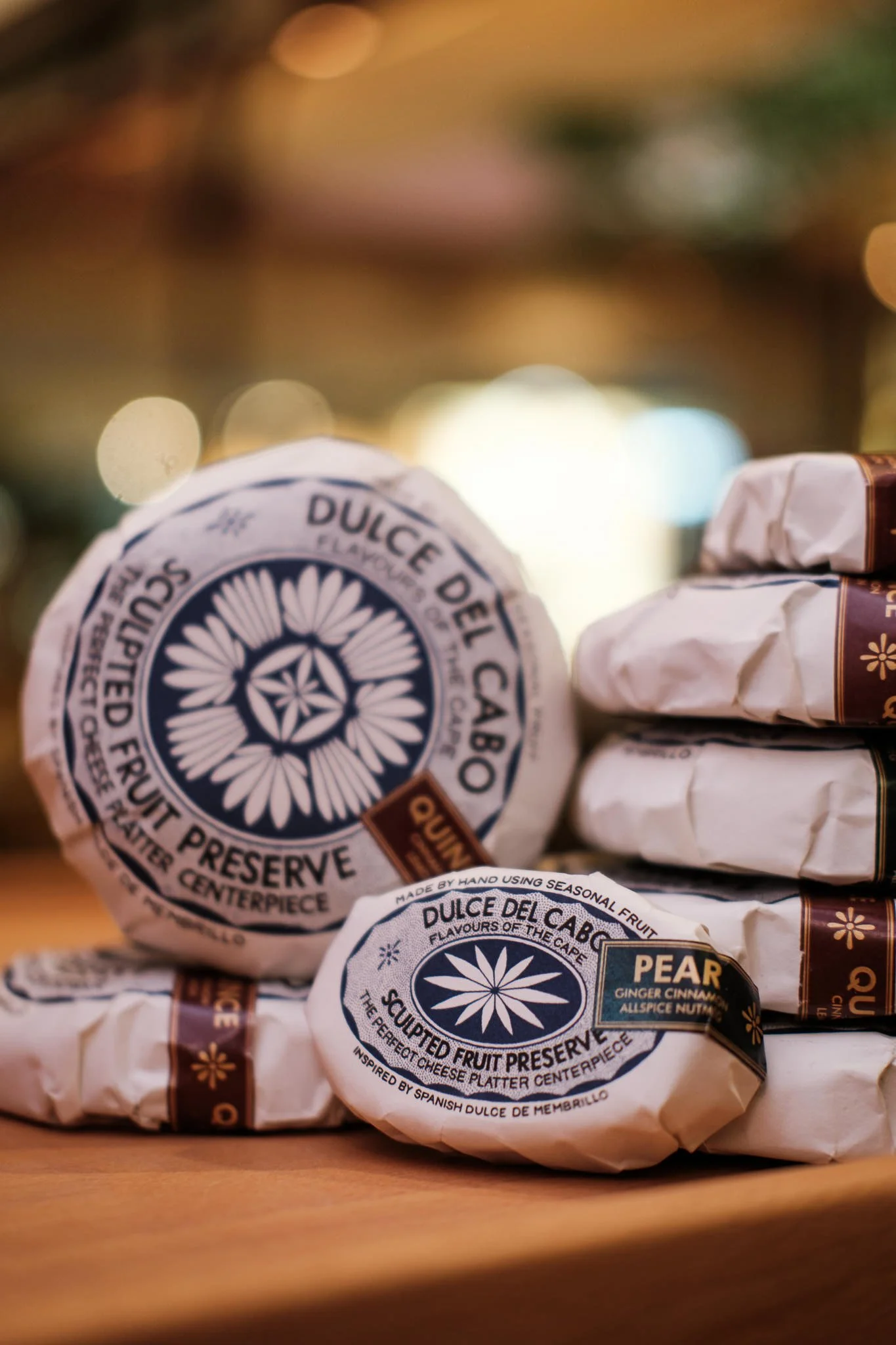 Wrapped fruit preserves with the label reading 'Dulce del Cabo' and mentioning flavors such as pear, ginger, cinnamon, and allspice, placed on a wooden surface.