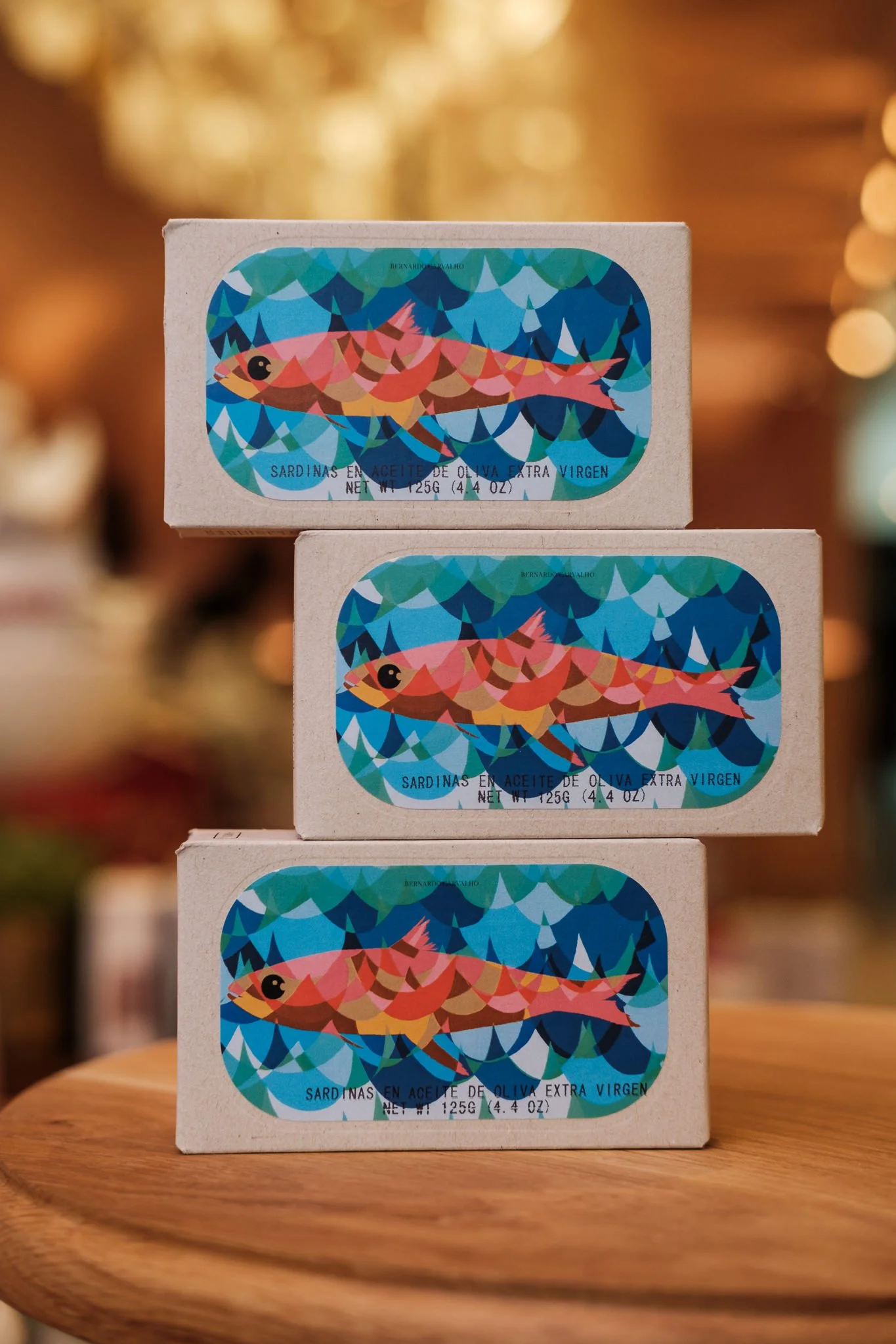 Boxes of sardines stacked on a wooden table with a blurred warm-colored background.