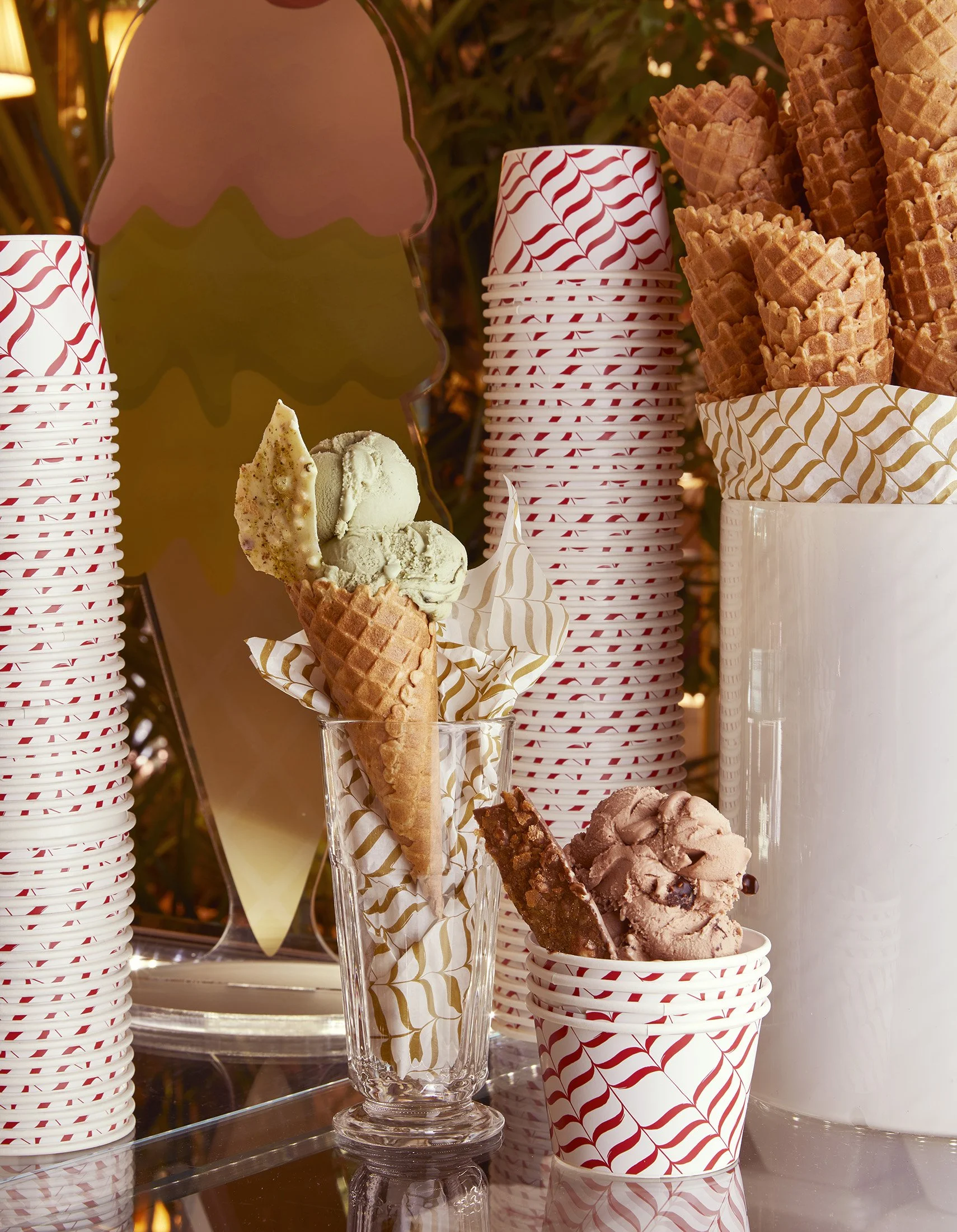 Ice cream cones in a display with red and white striped cups, some cone on top of paper with red and white swirl pattern, and a decorative mirror in the background.