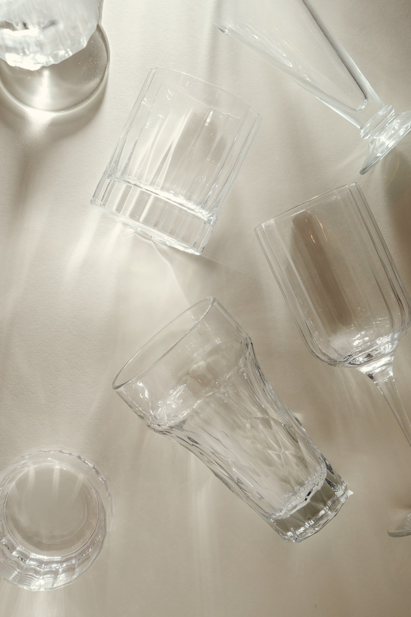 Multiple clear glass drinking glasses arranged on a light-colored surface, with some glasses upright and others tilted or lying down.